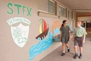 Two students at St Francis Xavier's Catholic Primary School Lurnea walking and smiling in front of mural